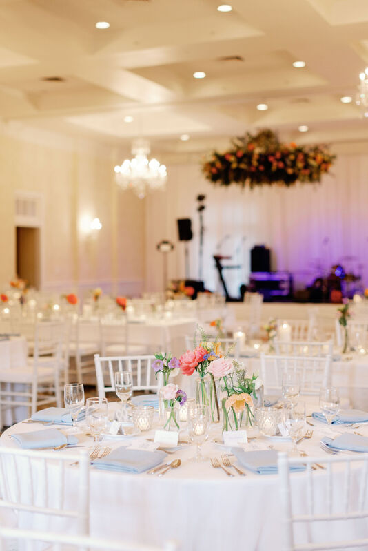 Indoor Reception, Wide Room Shot, Hanging Floral Install, Dance Floor, White Stage for Band, Pink Peonies, Yellow Roses, white Roses, Peach Roses, Lavender, Purple Flowers, Greenery, Clear Gold Rimmed Votives, White Linens, White Chivari Chairs, Light Blue Napkins, Pops of Color amidst White and Carolina Blue, Wedding Details, Wedding Decor, Silverware, Clear Glassware, Menu Card, Bread and Butter Plate, Cape Fear Country Club, Knot Too Shabby Events, Wilmington Wedding Planner, NC Wedding Planer, 