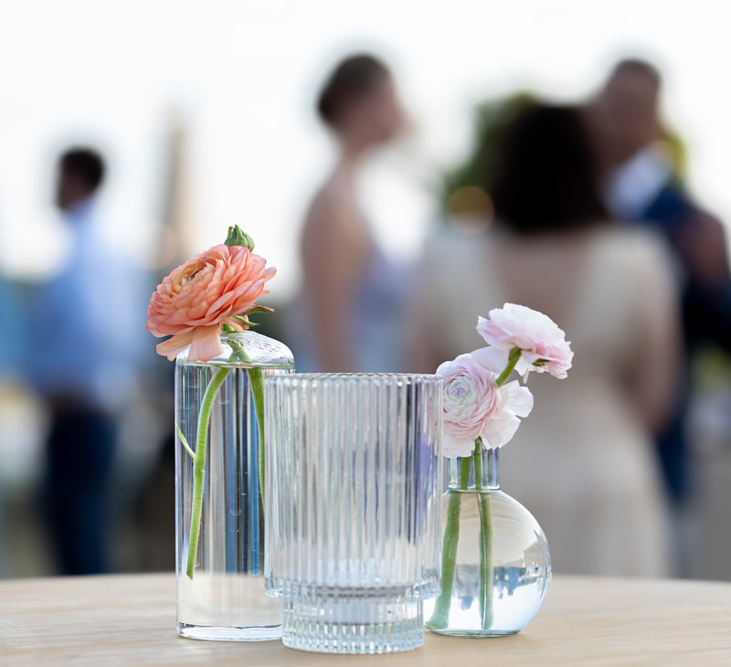 Knot Too Shabby Events, NC Wedding Planner, NC Wedding Coordinator, Bald Head Island Wedding, Summer Wedding, Pink, Blue, White, Coastal Chic, Elegant, Coral, Teal, Clear bud vases with coral and light pink flowers along with a clear ribbed votive sitting on a wooden top of a cocktail table. 