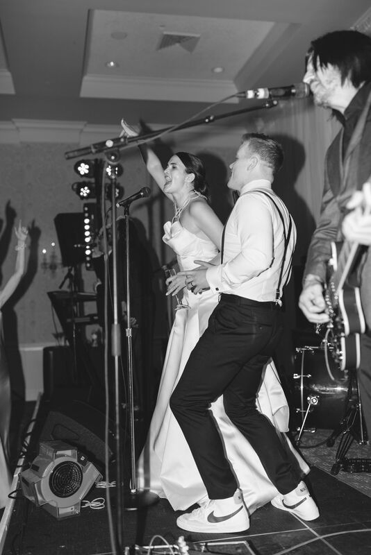 Bride and Groom on Stage, Black and White Photography, Indoor Reception, Dance Party, Live Band, Wedding Band, Reception Vendor, End of the Night, White Strapless Wedding Dress, Black Suit without Jacket, Black Bow Tie, Black Suspenders, Cape Fear Country Club, Knot Too Shabby Events, Wilmington Wedding Planner, NC Wedding Planner, 