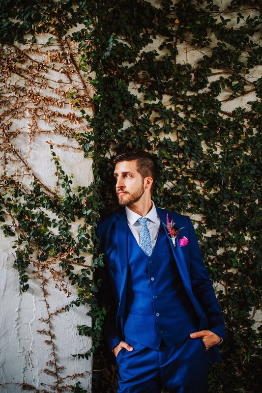 Groom, Gazing into the Distance, Blue Suit, Blue Tux, Leaning Against Venue, Greenery Wall, Natural Ivy, Indoor/Outdoor Venue, Wedding Day Photography, Blue Tie, Pink Flowered Boutonniere, Knot Too Shabby Events, Wilmington Wedding Planner, North Carolina Wedding Planner, 